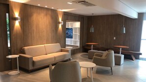 Un salon moderne avec un canapé, des fauteuils et une table basse. On y trouve des étagères murales et des luminaires suspendus.