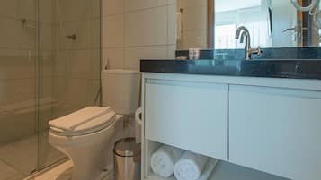 A modern bathroom with a glass shower enclosure, a white toilet, and a vanity with a mirror and sink.