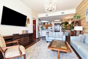 A living room with a flat-screen TV, a wooden coffee table, a blue sofa, and a chandelier.