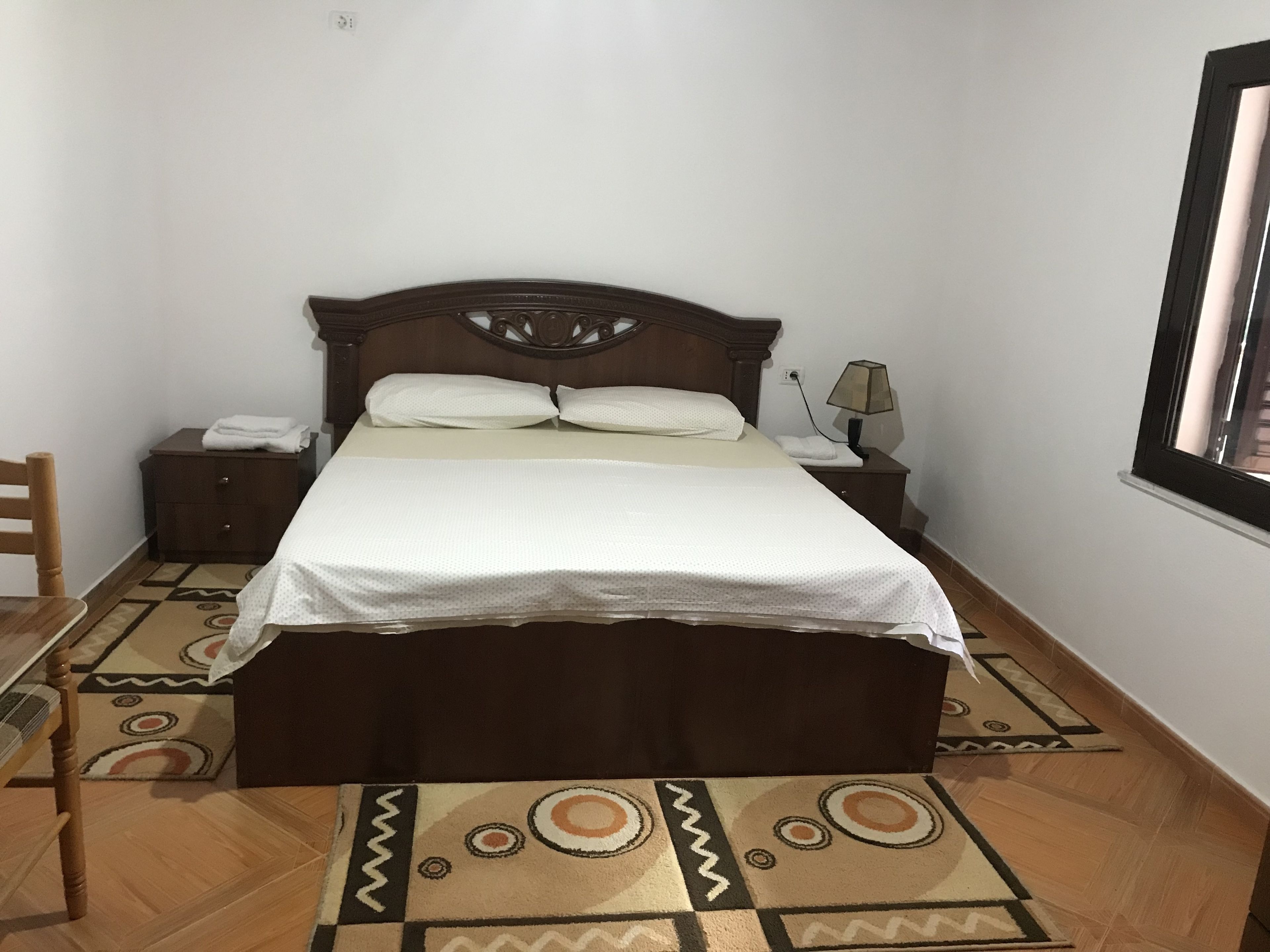 A neatly made bed with a wooden headboard, a bedside table with a lamp, and a chair.