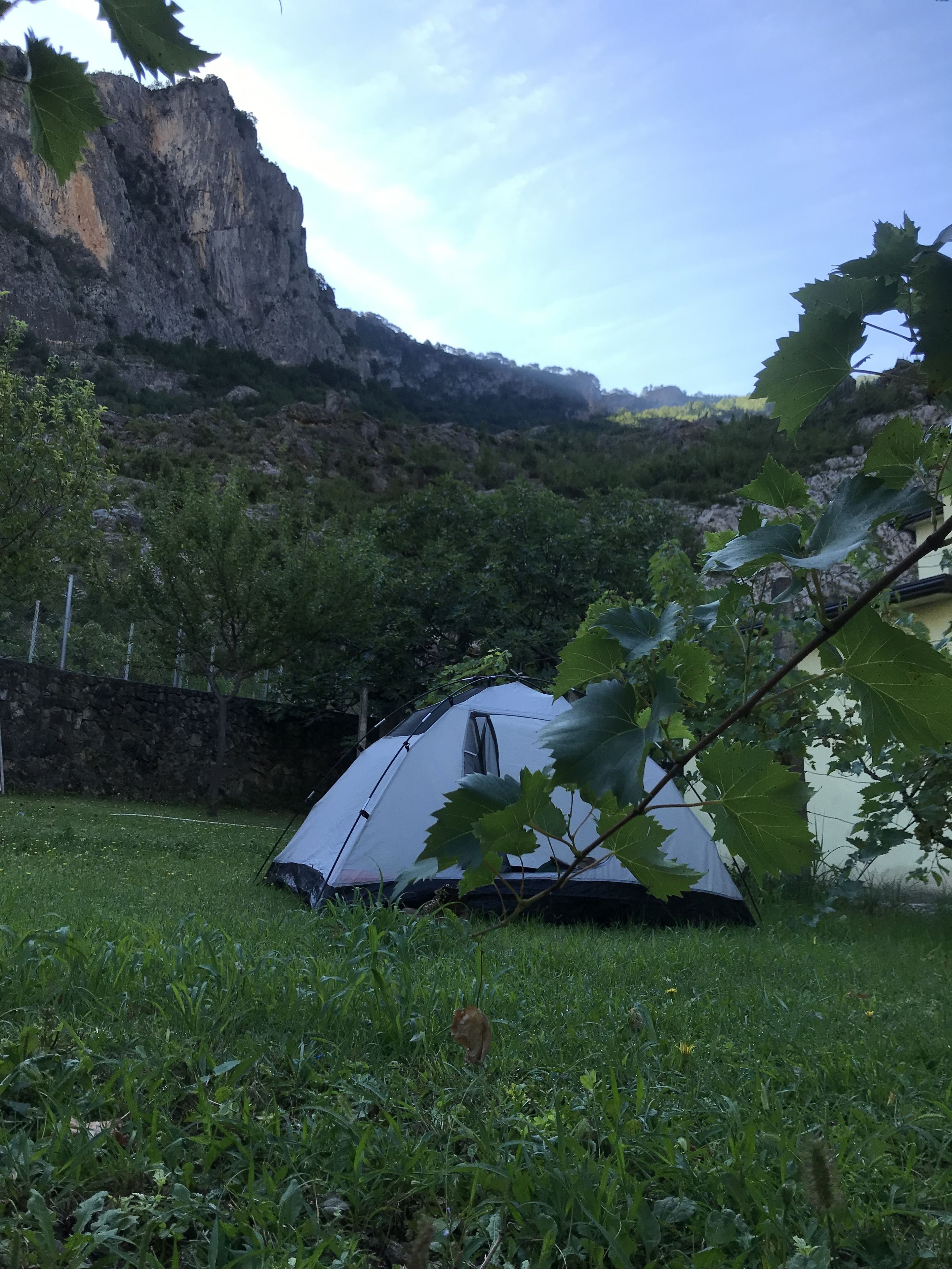 Una tienda de campaña montada en un área cubierta de césped, con una montaña rocosa al fondo.