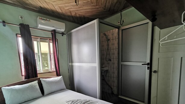 A bedroom with a bed, a window with curtains, an air conditioning unit, and a shower area. - Hôtel 2S (Douala)