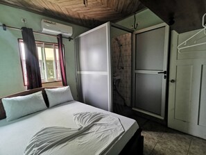 Ein Schlafzimmer mit Bett, einem Fenster mit Vorhängen, einer Klimaanlage und einem Duschbereich.