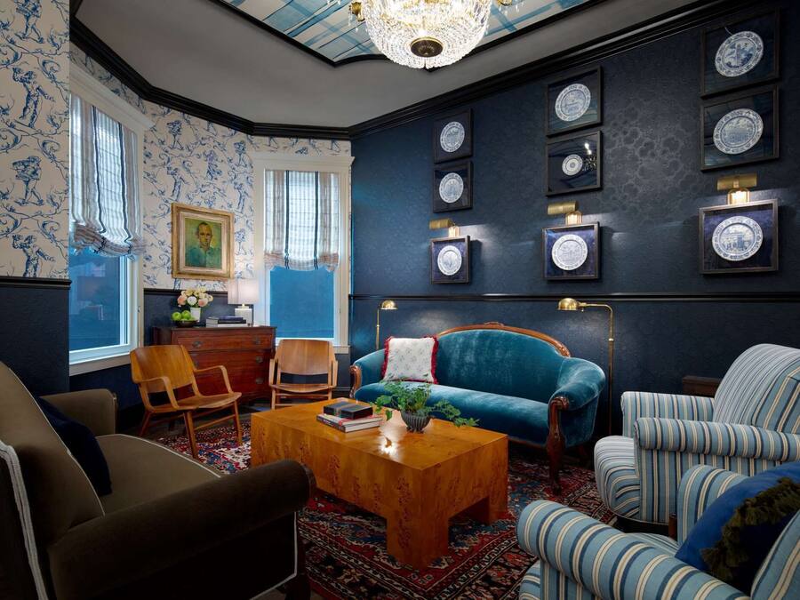 A room with a blue sofa, striped armchairs, a wooden coffee table, and a chandelier.