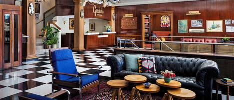 A lobby with a checkered floor, a black leather sofa, blue armchairs, and a chandelier.