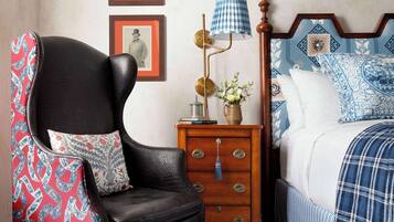 A bedroom with a black leather armchair, a wooden nightstand with a lamp, a bed with patterned bedding, and a wall with framed pictures.