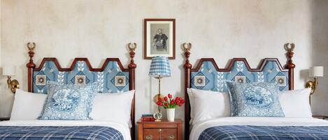 A double bed with a blue and white patterned headboard, a wooden nightstand with a lamp, and a framed picture on the wall.