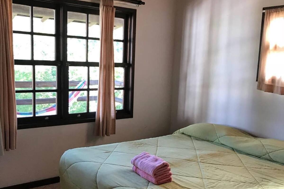 Une chambre avec un lit, une fenêtre avec des rideaux et une vue sur la verdure.