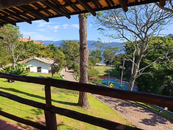 A view from a covered area overlooking a pool, a grassy area, and a building with a red roof. - Residencial Cabanas da Praia Mole (Florianópolis)