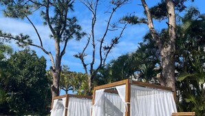 Outdoor seating areas with wooden benches and white canopies, surrounded by tall pine trees. - Residencial Cabanas da Praia Mole (Florianópolis)