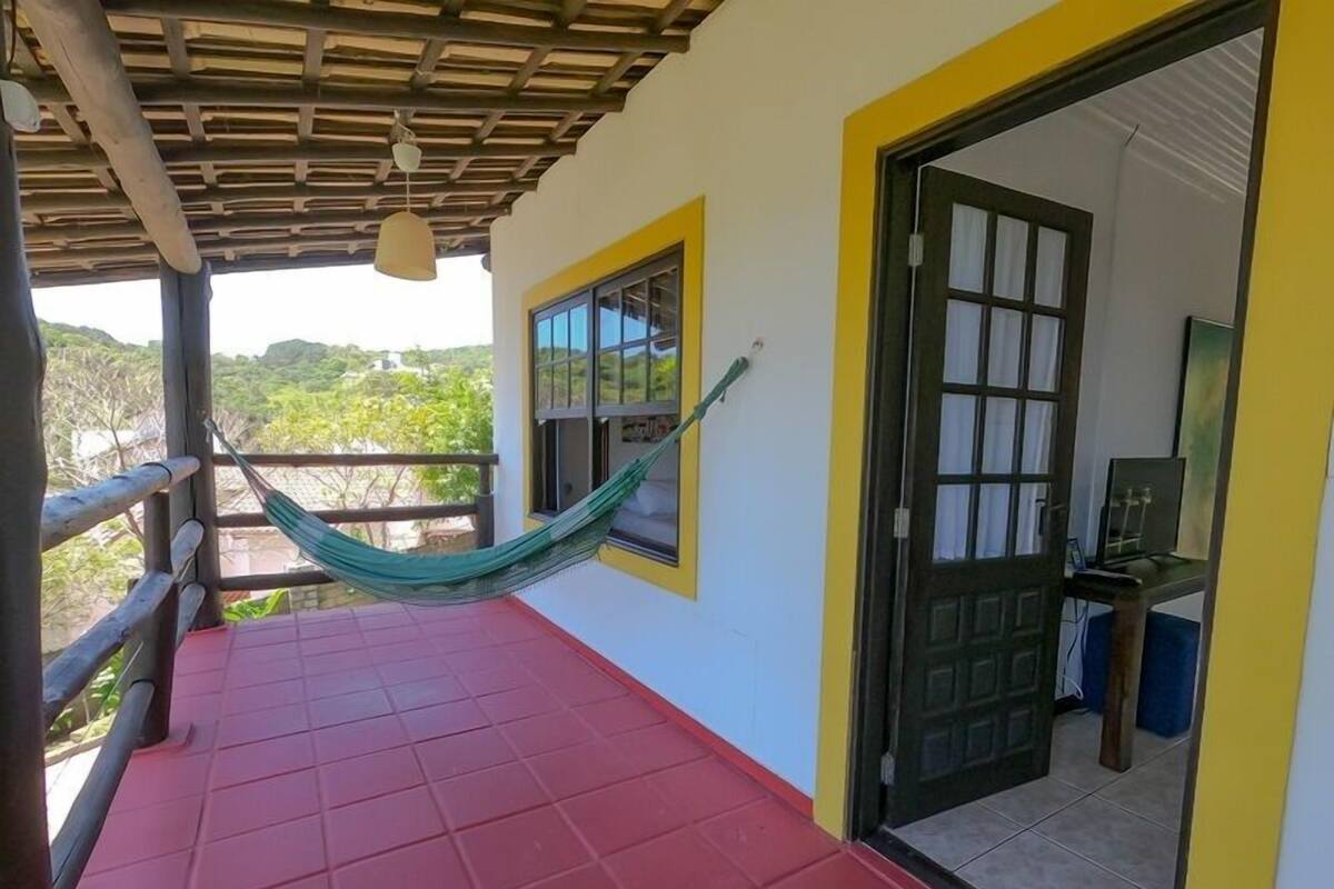 Un balcon doté d’un sol carrelé de tuiles rouges, d’un hamac et d’une porte donnant sur une pièce où se trouve un téléviseur.