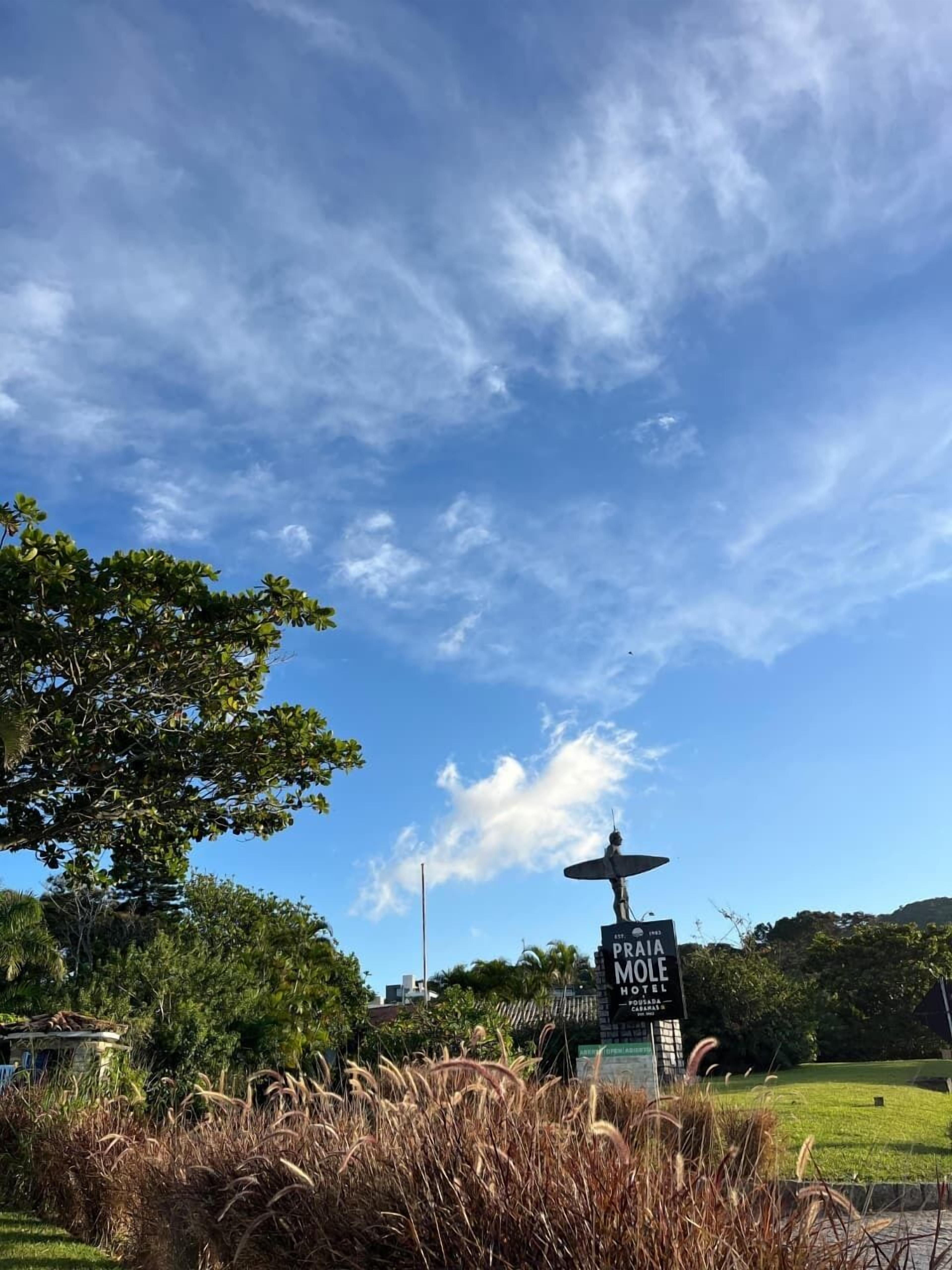 A sign for the Praia Hotel with a statue of a bird, surrounded by greenery and a clear sky.