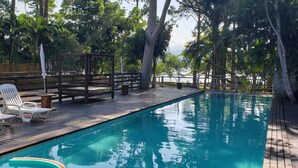 A wooden deck with a swimming pool, lounge chairs, and a wooden pergola. - Residencial Cabanas da Praia Mole (Florianópolis)
