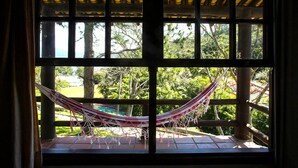 A hammock tied between two wooden beams, with a view of greenery and a building in the background. - Residencial Cabanas da Praia Mole (Florianópolis)