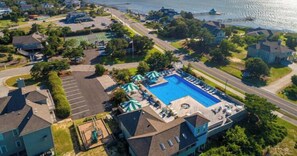 An aerial view of a residential area with a swimming pool, tennis courts, and a waterfront.