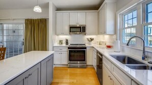 A modern kitchen with white cabinets, stainless steel appliances, and a large window providing natural light.