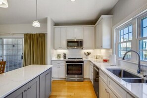 A modern kitchen with white cabinets, stainless steel appliances, and a large window providing natural light.