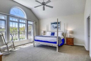 A bedroom with a large window, a bed, a ceiling fan, and a nightstand.