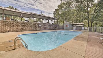 A swimming pool with a stone wall, a covered area with tables, and a small shed.