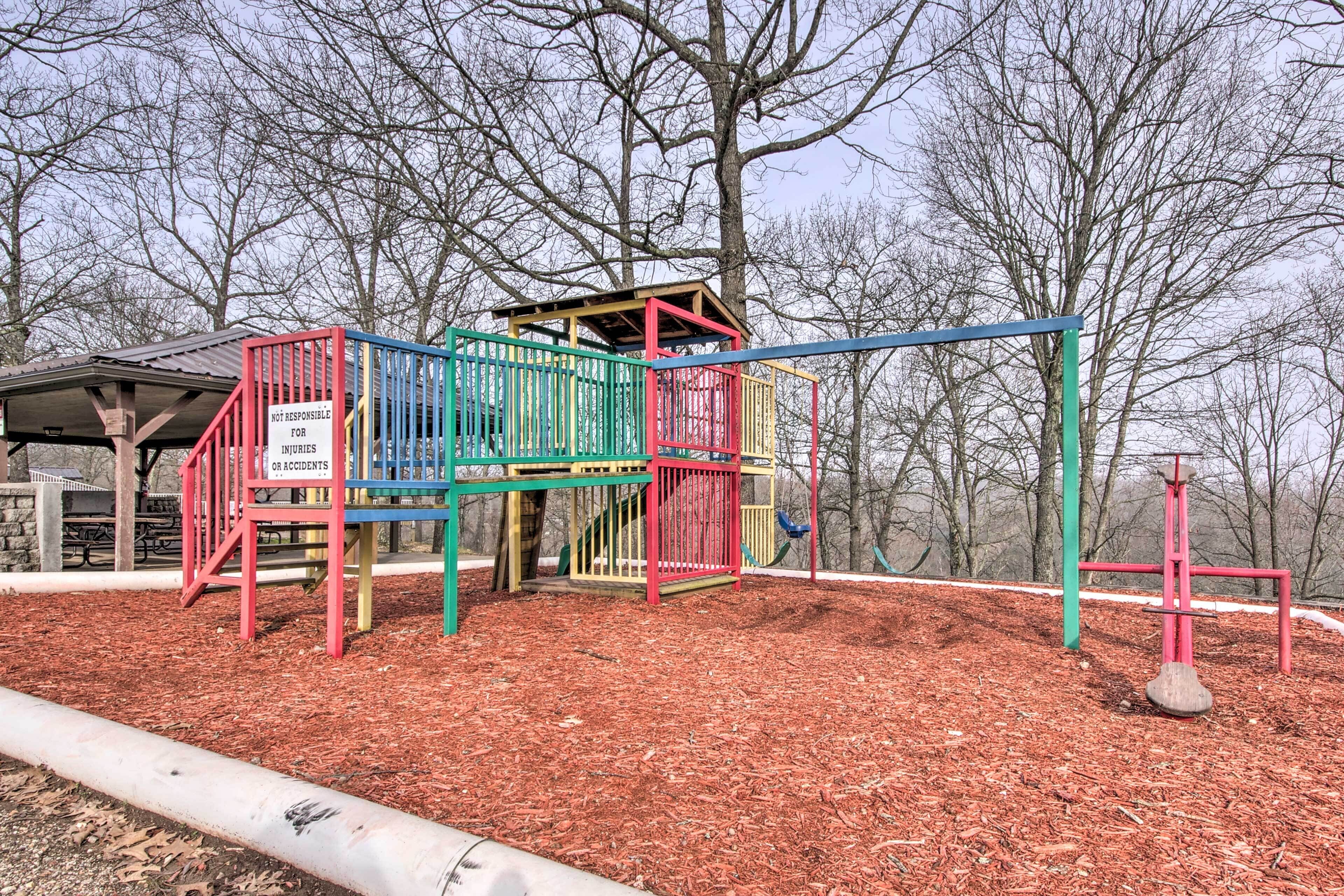 Une aire de jeux avec une structure d’escalade et une balançoire, entourée d’arbres et recouverte de paillis.