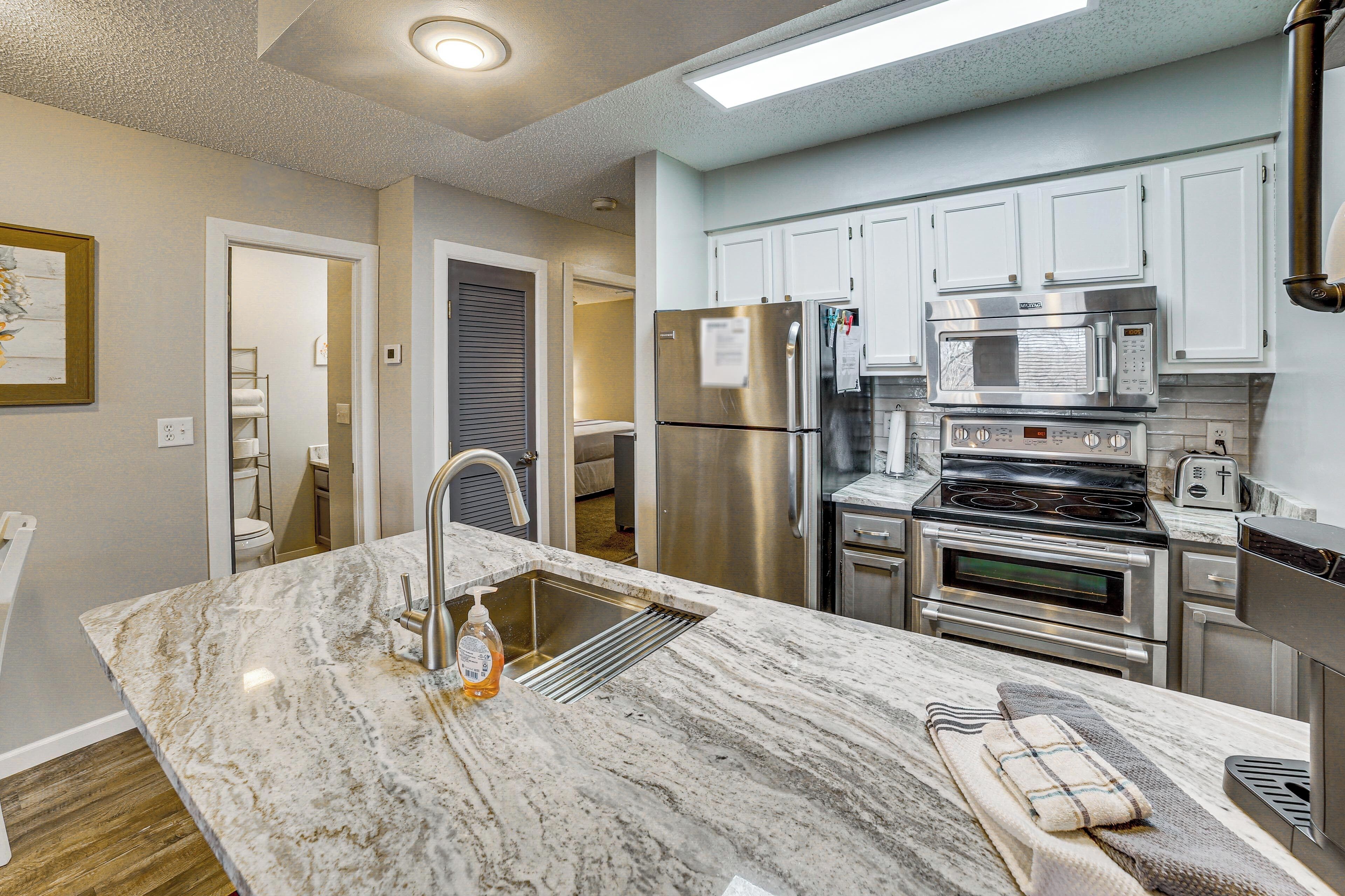 A modern kitchen with stainless steel appliances, a marble countertop, and white cabinetry.