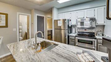 A modern kitchen with stainless steel appliances, a marble countertop, and white cabinetry.