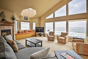 Relax in a spacious living room with a sofa, armchairs, flat-screen TV, and fireplace, offering a serene ocean view.