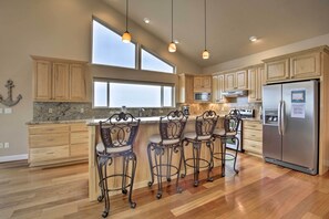 A modern kitchen with wooden cabinets, a stainless steel refrigerator, a granite countertop, and bar stools.