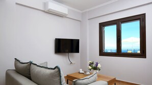 Een moderne woonkamer met een grijze bank, een houten salontafel, een flatscreen televisie en een raam met uitzicht op zee.