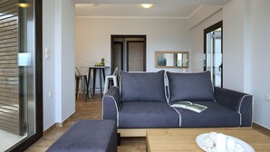 Een moderne woonkamer met een grijze bank, een houten salontafel en een glazen deur naar een balkon.