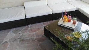 A section of a hotel room with a white cushioned bench along the wall, a glass-top coffee table with drinks and condiments, and a stone floor. - Villa Carmen (Mondragone)
