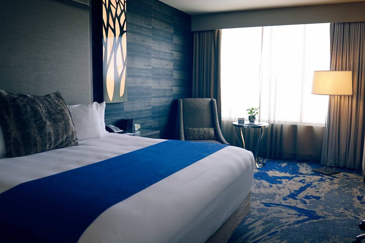 A hotel room with a large bed, a chair, a small table, and a lamp.