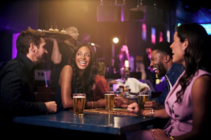 Un grupo de personas sentadas en un bar con bebidas, en un ambiente interior con poca luz.