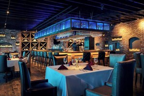 Un restaurant avec des tables dressées pour le service, un bar avec un barman et un mur en briques en arrière-plan.