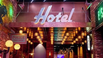 L’entrée d’un hôtel, avec une enseigne au néon, un panneau indiquant la présence de la police et une enseigne pour un salon de coiffure.