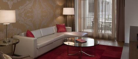 A modern hotel room with a sofa, a glass coffee table, and two lamps.