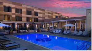Un hotel con piscina, sillas de descanso y sombrillas.