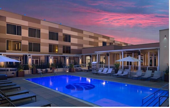 A hotel with a swimming pool, lounge chairs, and umbrellas.