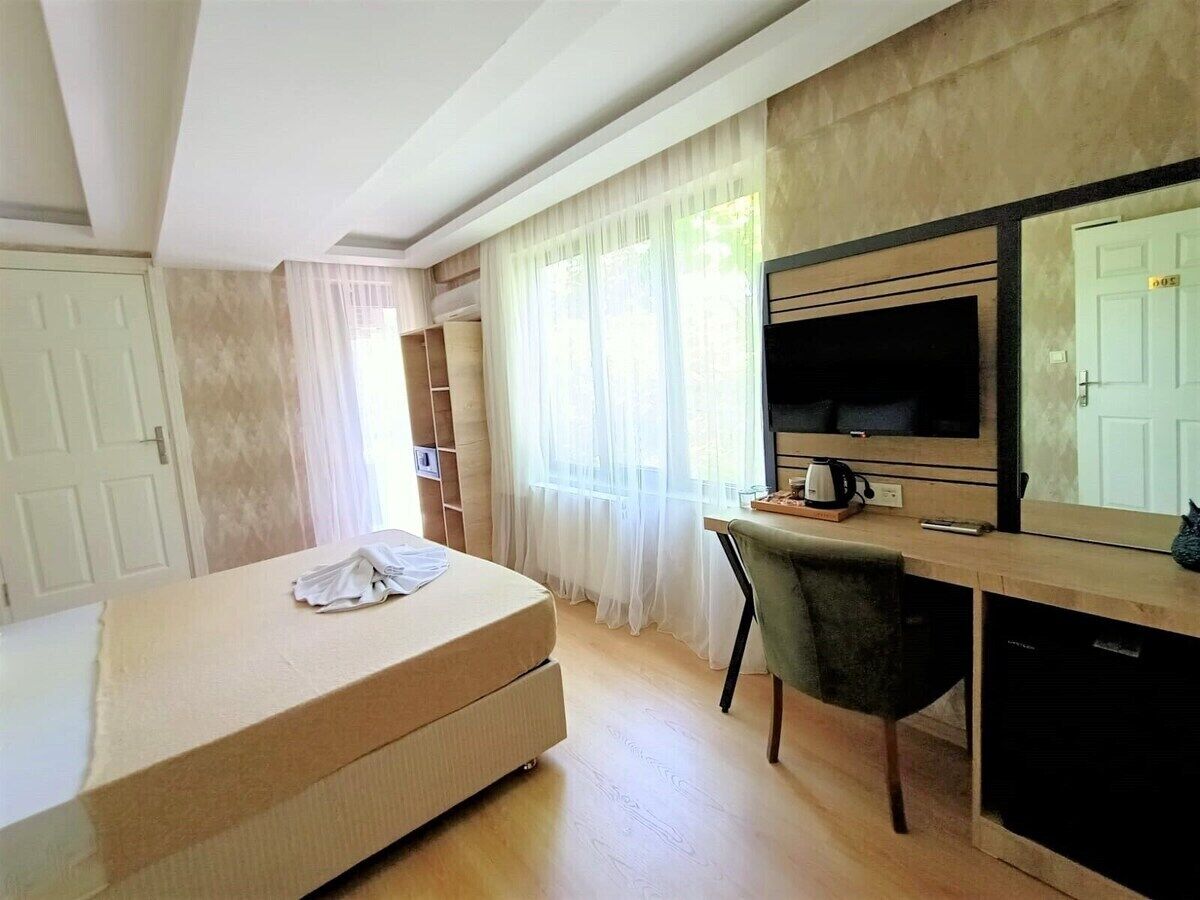 Una habitación con cama, escritorio, silla, televisión y espejo.