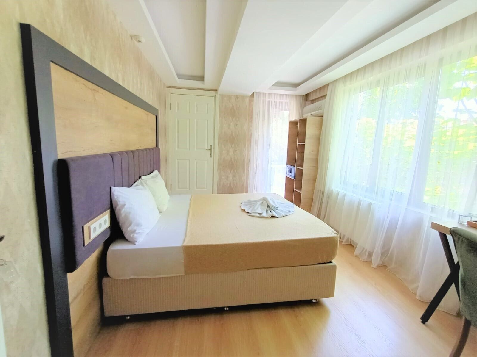 A bedroom with a bed, a chair, a wardrobe, and a window with curtains.