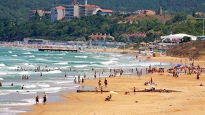 A beach with people swimming and sunbathing, a pier, and buildings in the background. - Avcilar Elit Hotel (Istanbul)