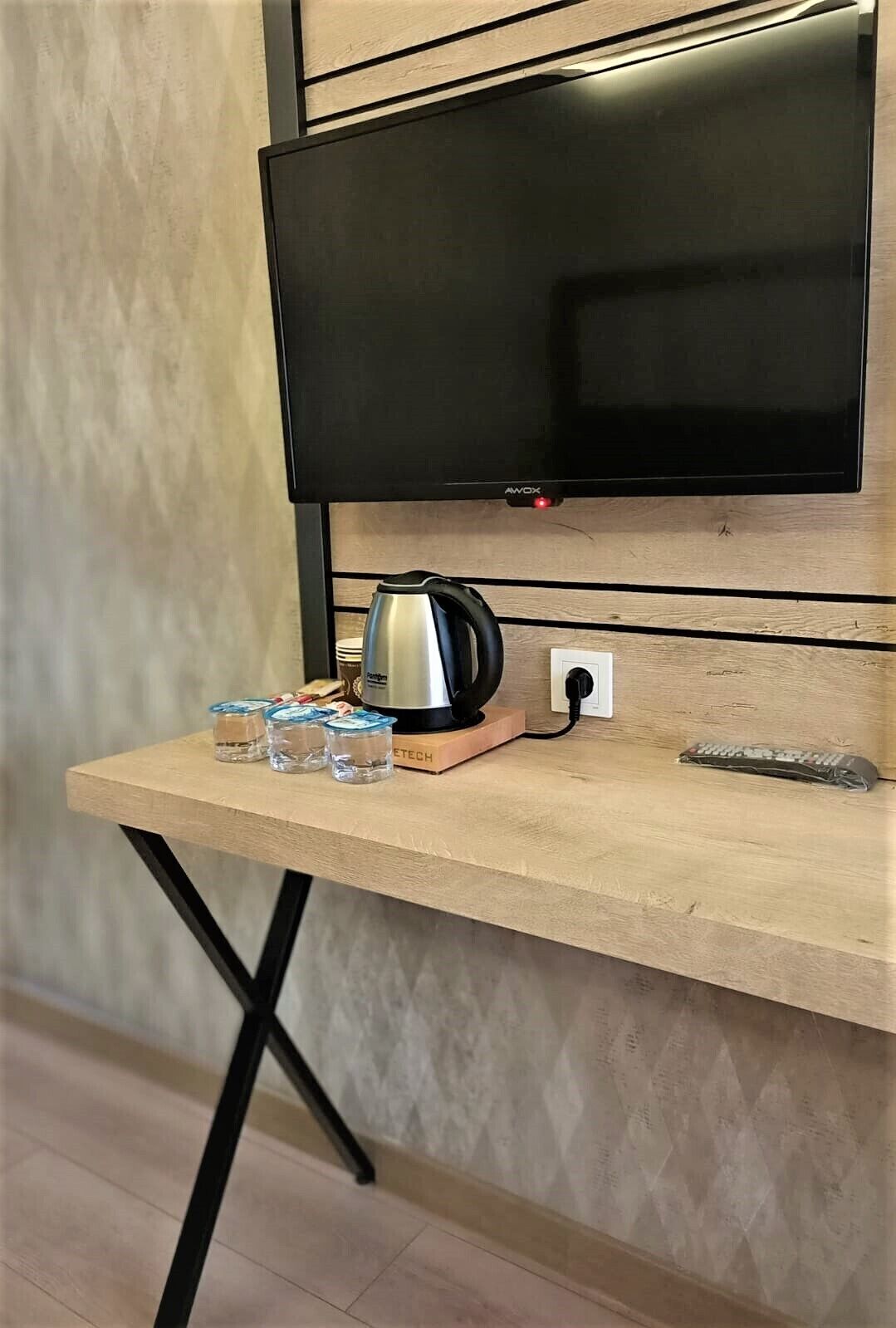 A wooden desk with a kettle, glasses, and a remote control.