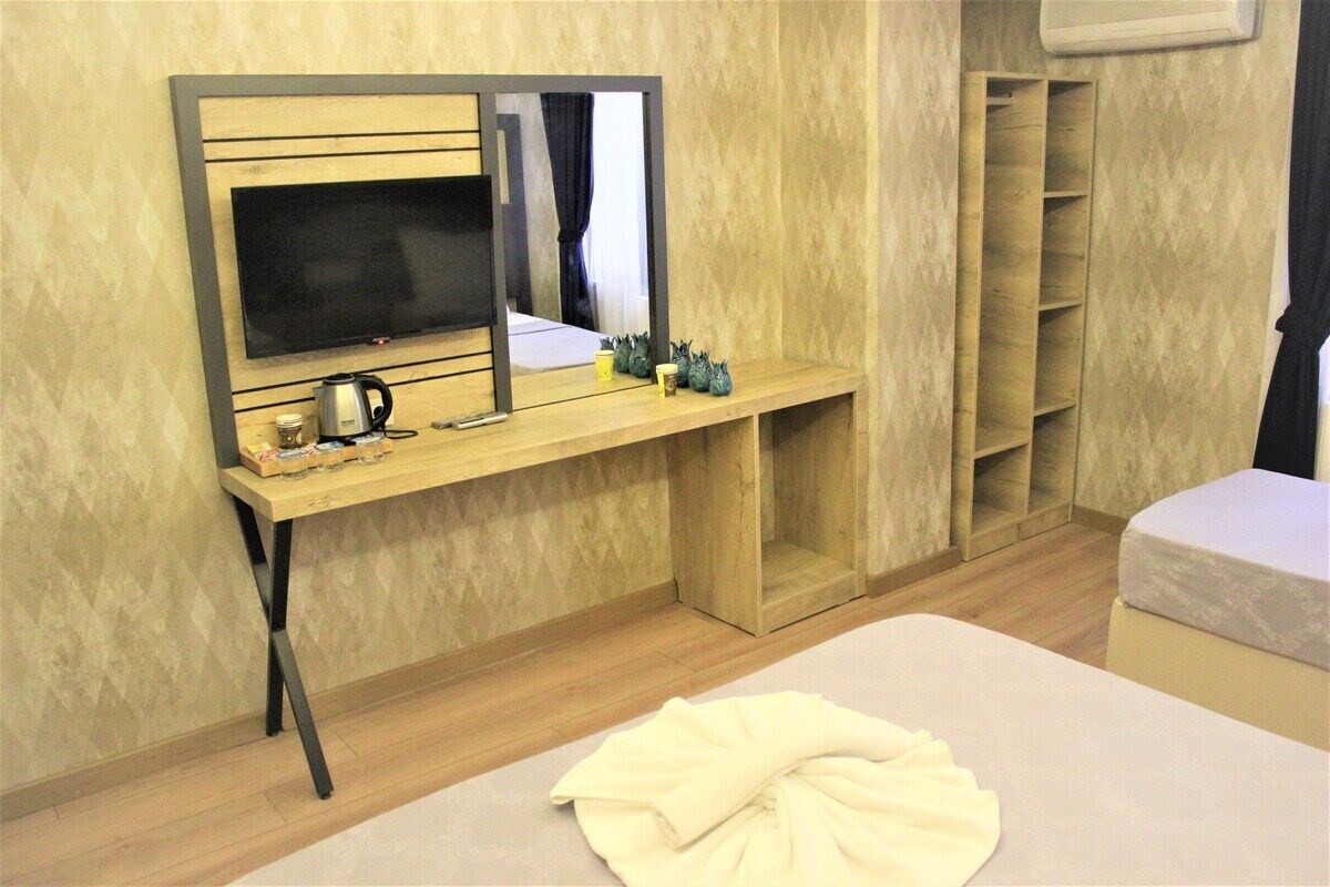 Une chambre d’hôtel comprenant un lit, un bureau avec un téléviseur à écran plat, un miroir, une machine à café et une étagère avec des objets décoratifs.