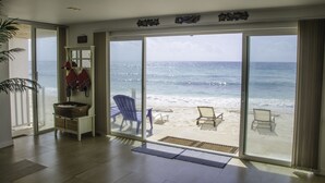 A room with a large sliding glass door leading to a beach view, a wicker basket, a blue chair, and a wooden bench. - Penelope Beach House (San Andrés)