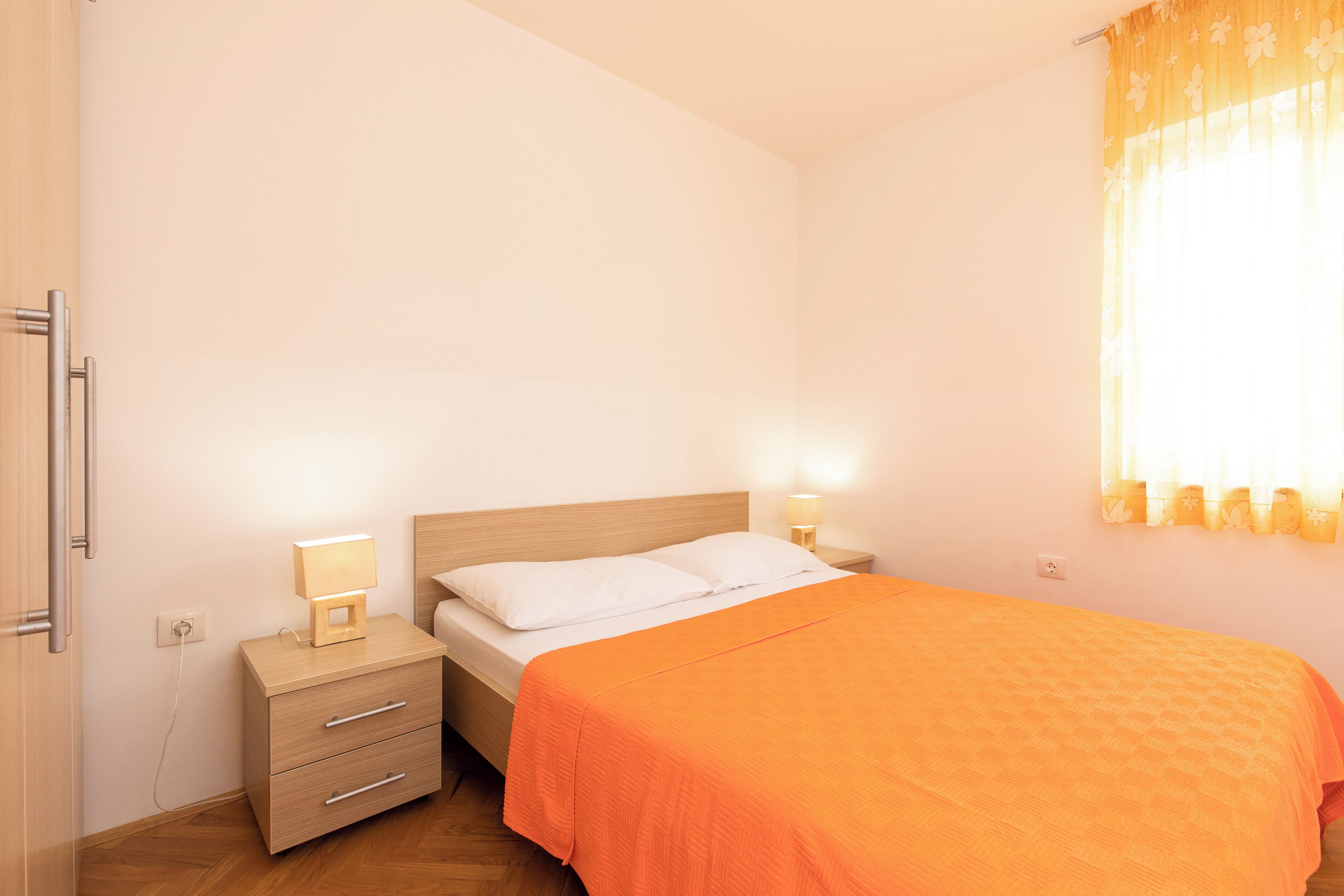 A bedroom with a bed, bedside tables, a nightstand, a lamp, and a window with curtains.