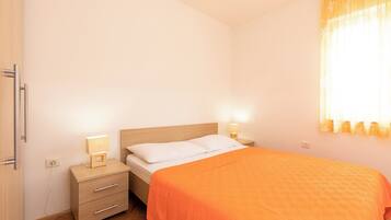 A bedroom with a bed, bedside tables, a nightstand, a lamp, and a window with curtains.
