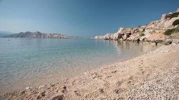 A pebble beach with clear water and rocky hills in the background.