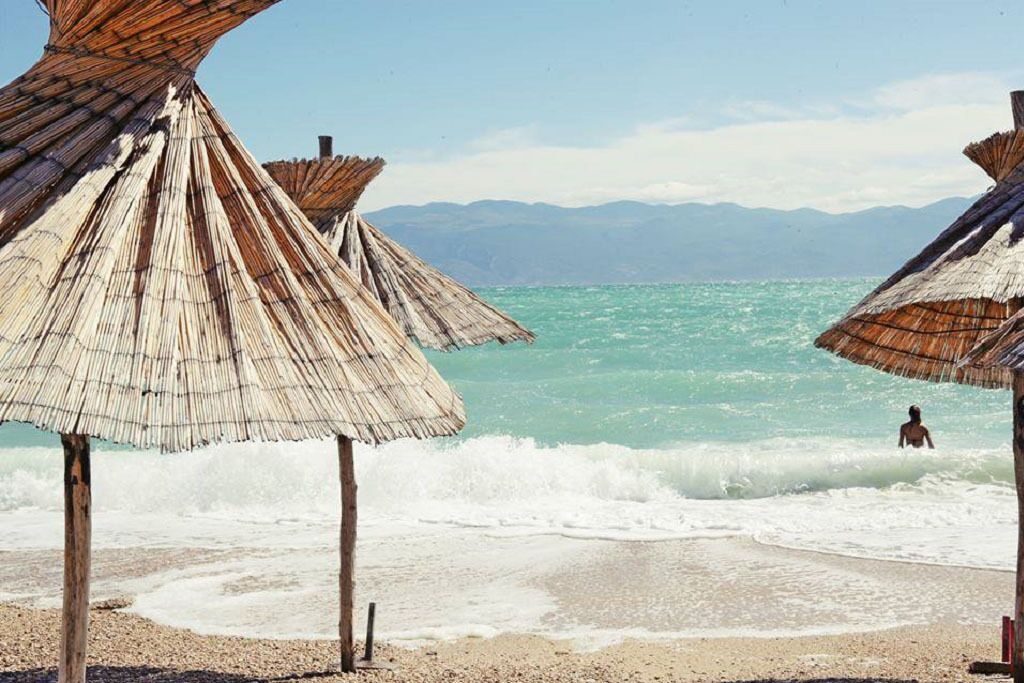 A beach with thatched umbrellas and a person in the water.