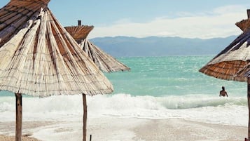 A beach with thatched umbrellas and a person in the water.