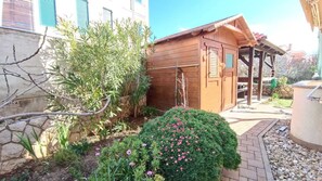 Una construcción de madera con puerta y ventana, rodeada por un jardín con diversas plantas y flores.